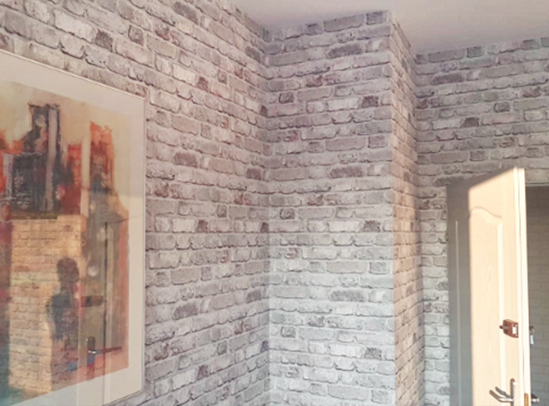 Wnętrze pokoju z tapetą imitującą białą cegłę, obraz w ramie na ścianie, otwarte białe drzwi po prawej.