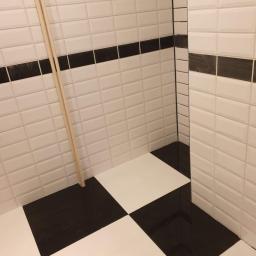 Gol-Bud - Wykończona łazienka z czarno-białymi płytkami w szachownicę na podłodze i białymi, prostokątnymi płytkami z czarnym paskiem na ścianach, oparta o ścianę listwa przypodłogowa.