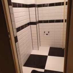 Gol-Bud - Czarno-biała łazienka w trakcie wykańczania: ułożone płytki w stylu retro, widoczny pojemnik z narzędziami glazurniczymi, fragment rury i przygotowane przyłącza wodne.