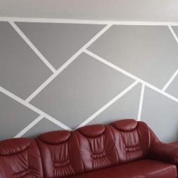 Gol-Bud - Szara ściana z geometrycznym wzorem z białych pasów, uzupełniona o czerwoną skórzaną sofę i głośniki po bokach, tworząca nowoczesną aranżację wnętrza.