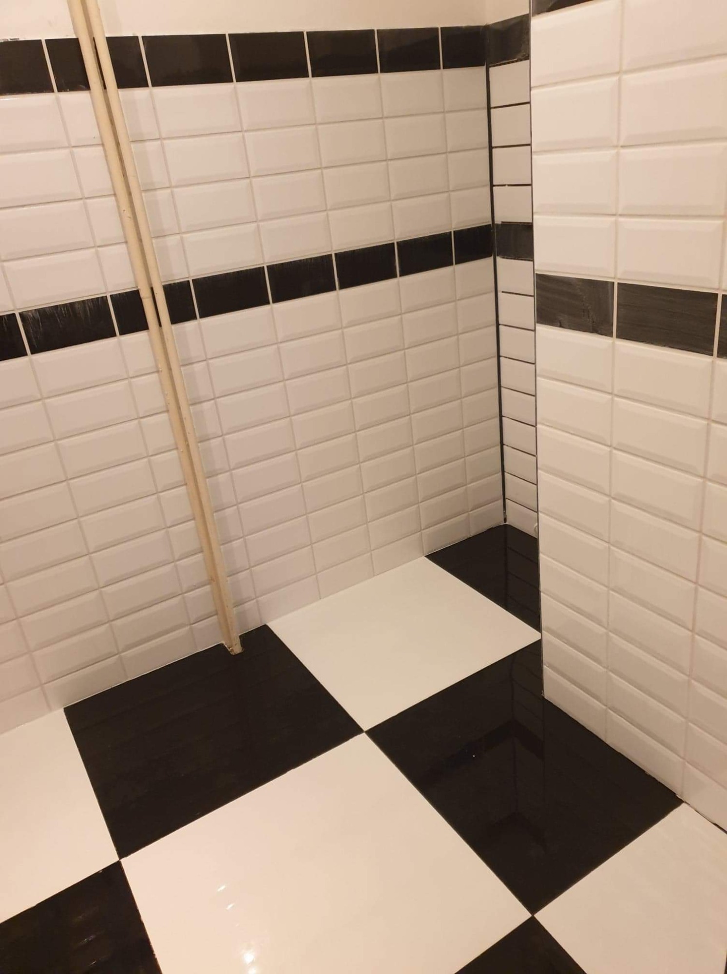 Wykończona łazienka z czarno-białymi płytkami w szachownicę na podłodze i białymi, prostokątnymi płytkami z czarnym paskiem na ścianach, oparta o ścianę listwa przypodłogowa.