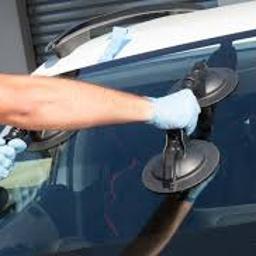 GLASS.O.S AUTO SZYBY - Pracownik w niebieskich rękawicach za pomocą dwóch przyssawek montuje nową szybę samochodową, widoczne narzędzia i elementy mocujące.