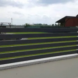 Nowoczesne ogrodzenie z poziomych, grafitowych profili metalowych, zamontowane na niskim murku z jasnego tynku i szarego granitu.