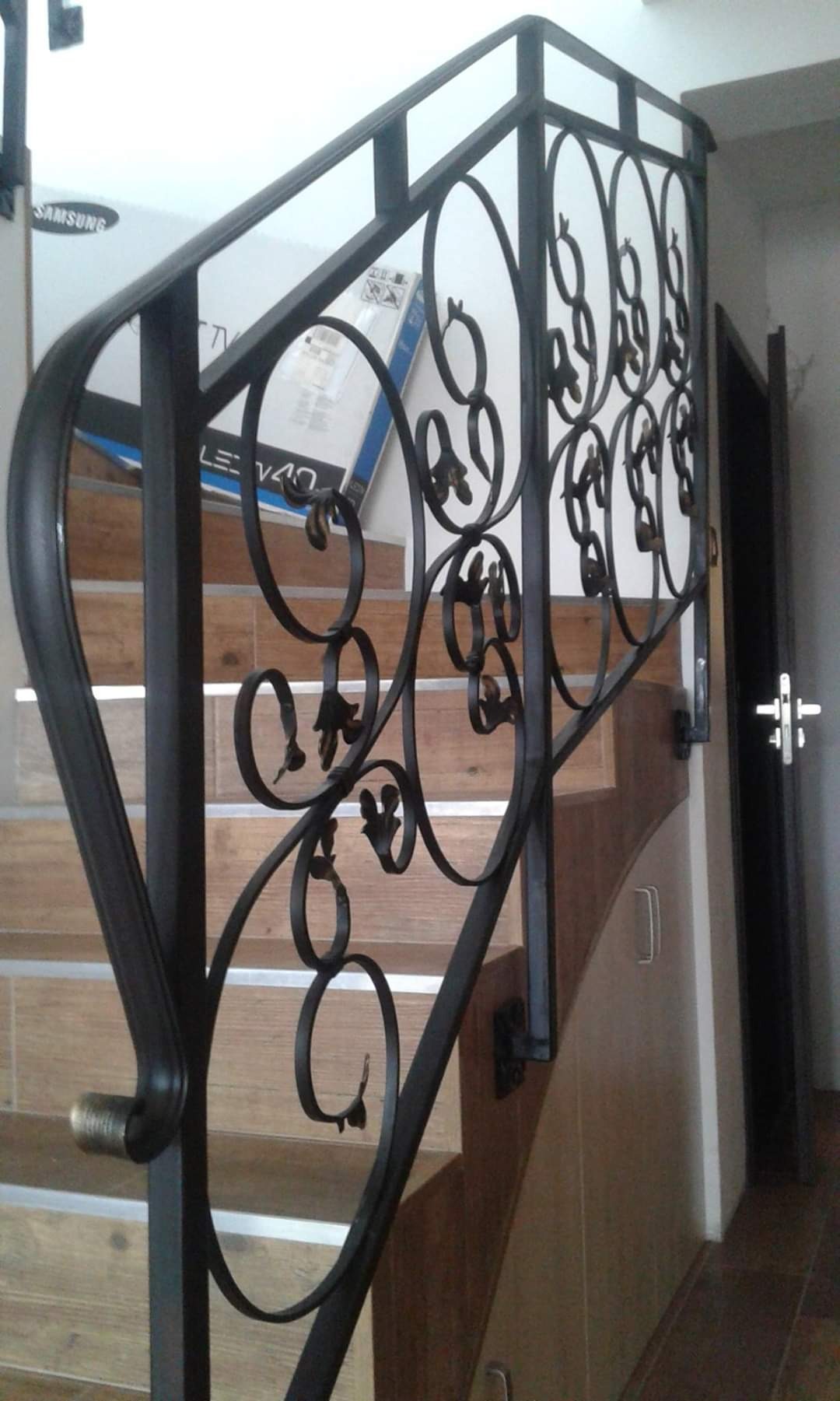 Kute, czarne balustrady schodowe z motywem roślinnym, drewniane schody z metalowymi paskami antypoślizgowymi, widok z dołu.