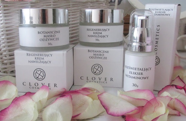 Zestaw kosmetyków marki Clover Cosmetics: botaniczne masło odżywcze, regenerujący krem nawilżający i rozświetlający eliksir witaminowy, otoczone płatkami róż.