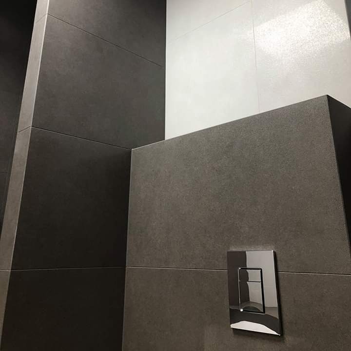 Szare i białe płytki w łazience z chromowanym przyciskiem spłuczki, minimalistyczny design.