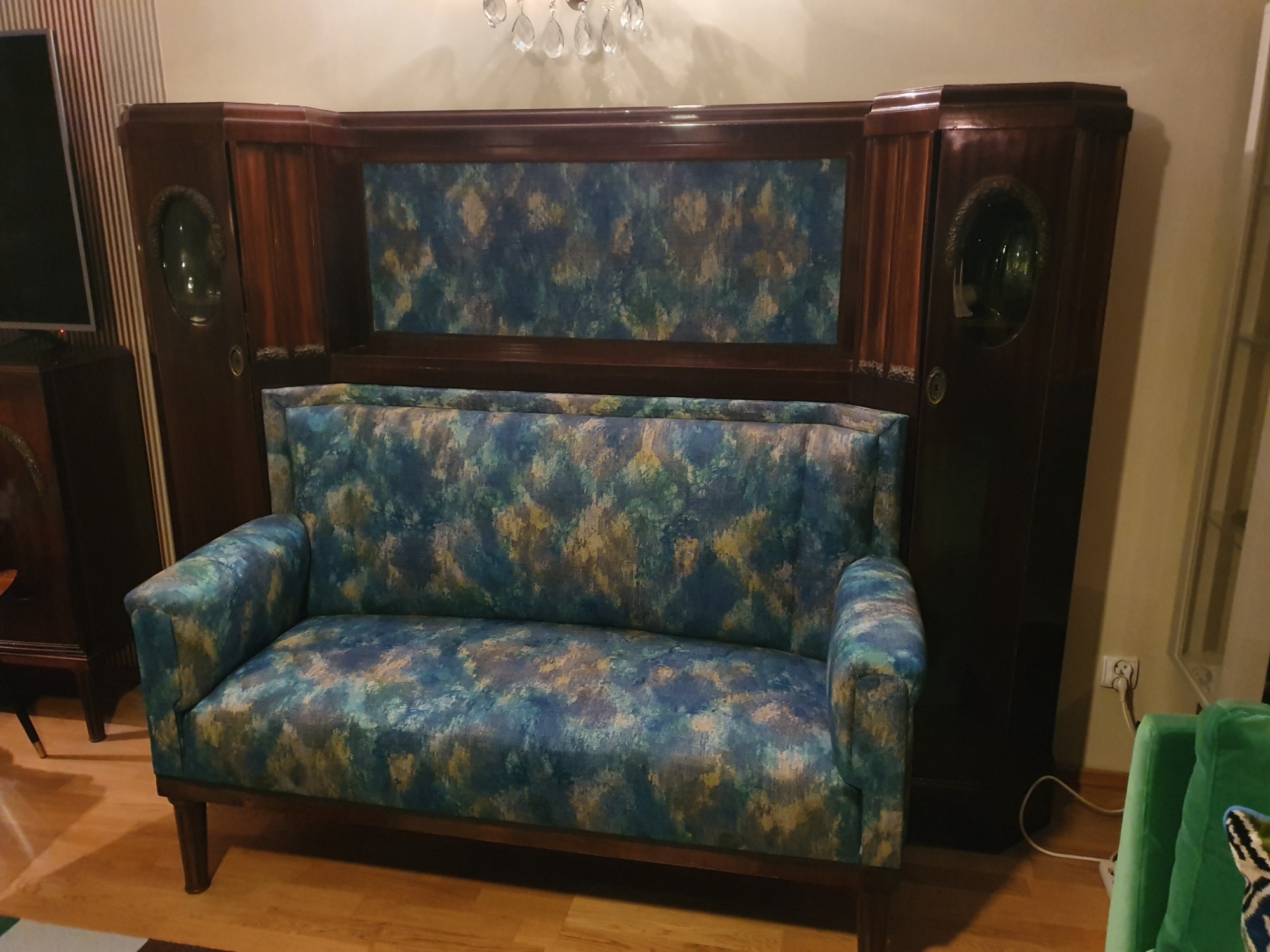 Odnowiona kanapa w stylu art deco z tapicerką w odcieniach błękitu i złota, umieszczona na tle drewnianej zabudowy z szafkami i dekoracyjną ścianką.