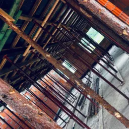 Wnętrze w trakcie budowy: czerwona cegła, drewniana konstrukcja dachu z widocznymi belkami i metalowymi podporami, surowe ściany, widok z dołu do góry.