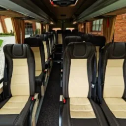 Wnętrze luksusowego busa z beżowo-brązowymi skórzanymi fotelami, widok na przejście i okno dachowe.