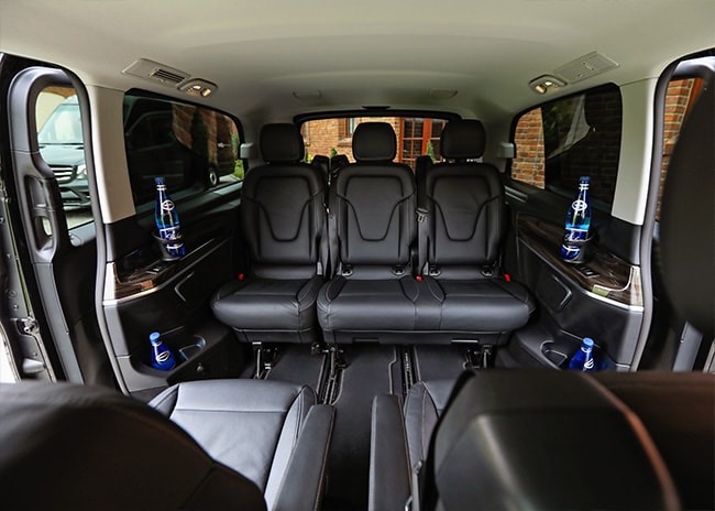 Wnętrze luksusowego vana z trzema rzędami skórzanych foteli, butelki wody mineralnej w uchwytach