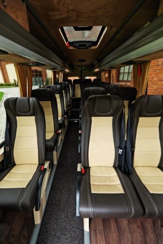 Wnętrze luksusowego busa z beżowo-brązowymi skórzanymi fotelami, widok na przejście i okno dachowe.