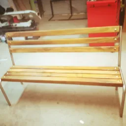 Metalowa ławka z drewnianym siedziskiem i oparciem, wykonana w warsztacie, widoczne ślady obróbki.