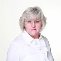 Portret kobiety w białej koszuli z falbankami, na jasnym, rozmytym tle.