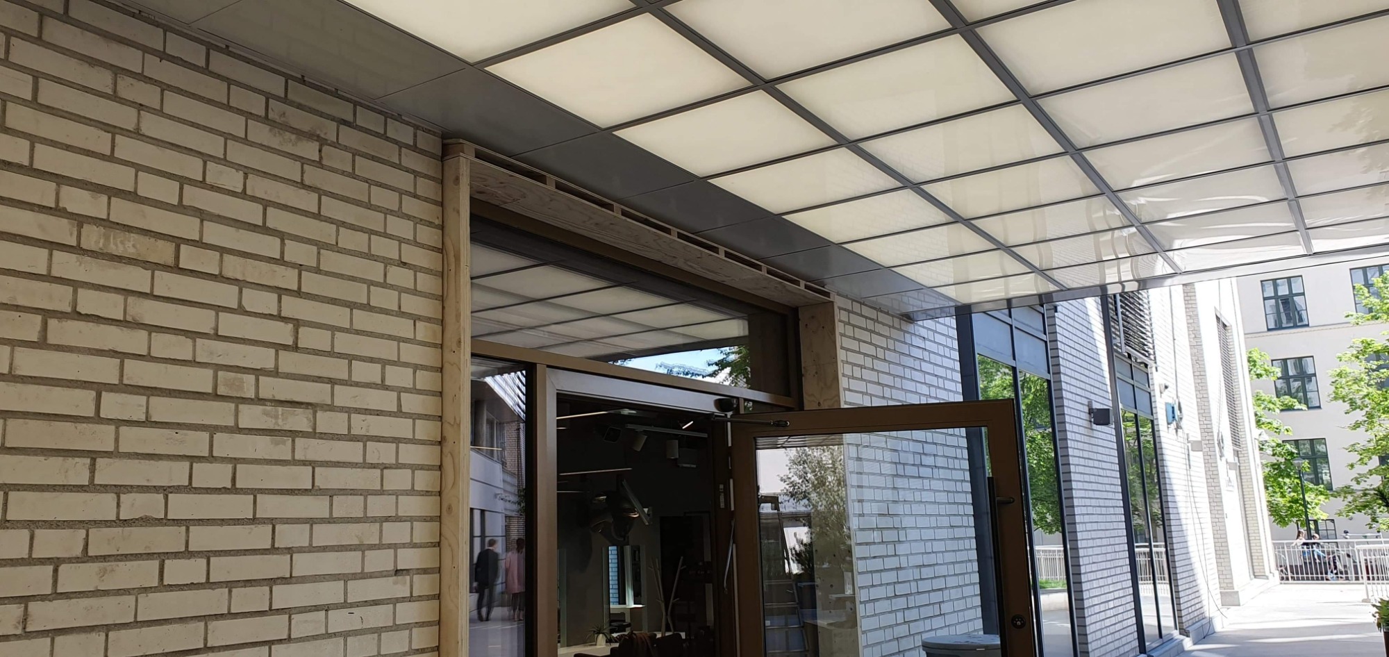 Otwarty, przeszklony portal wejściowy do budynku biurowego z białej cegły, z podwieszanym kasetonowym sufitem i widocznym wnętrzem.