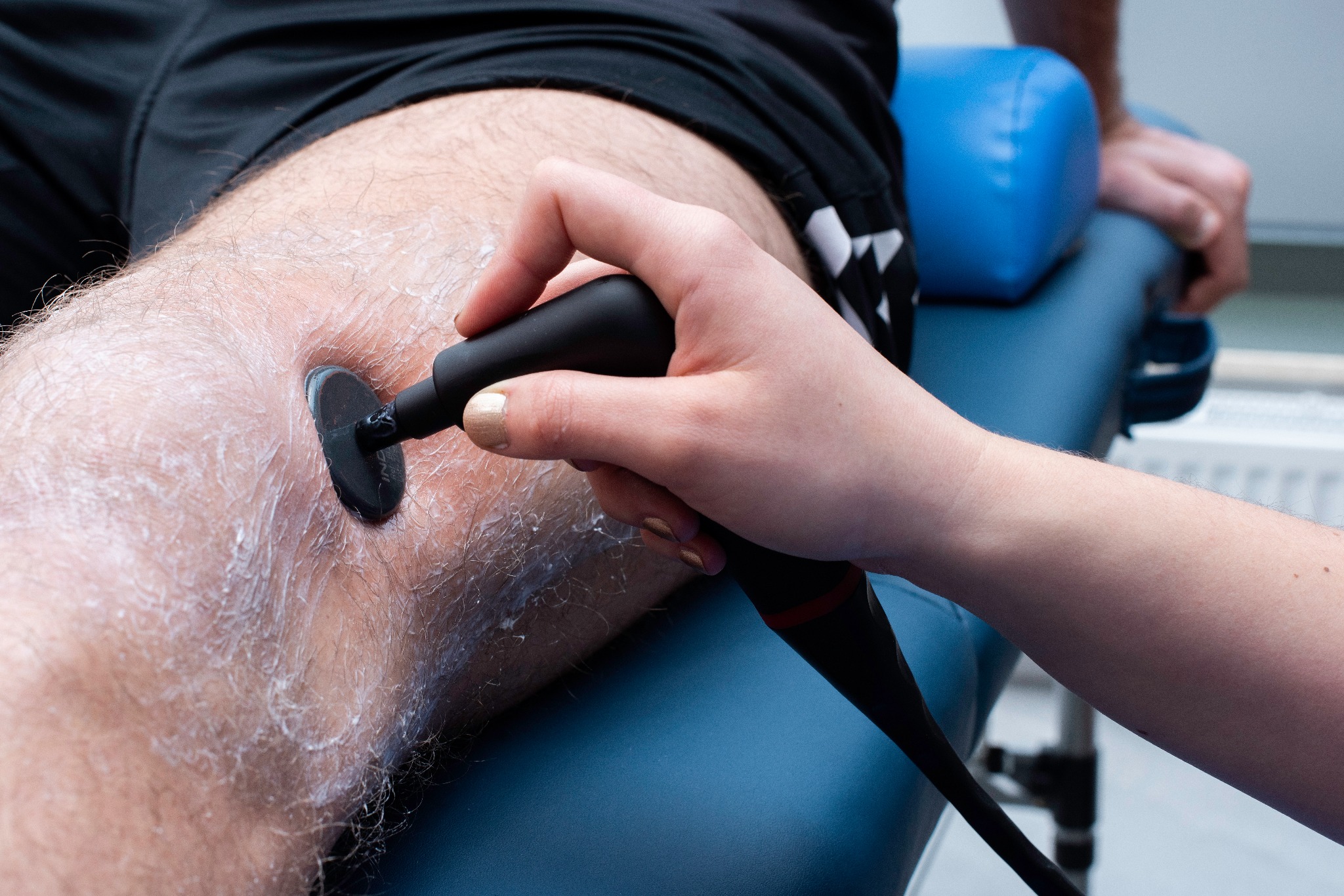 Ultradźwięki na kolano pacjenta z użyciem żelu, wykonywane przez terapeutę na niebieskim łóżku rehabilitacyjnym.