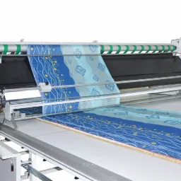 Automatyczna maszyna do rozkładania i cięcia tkanin z niebieskim wzorem, widoczny panel sterowania i system podawania materiału.