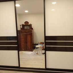 Wojciech Kozłowski - Nowoczesna szafa wnękowa z przesuwnymi drzwiami, dzielonymi poziomymi pasami w kolorze białym i ciemnobrązowym. W lustrzanym odbiciu widoczny antyczny kredens.