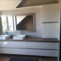 Wojciech Kozłowski - Nowoczesna łazienka w jasnych barwach: białe szafki pod umywalki nablatowe, duże lustro w szarej ramie, drewniany blat i płytki imitujące kamień. Minimalistyczny design.