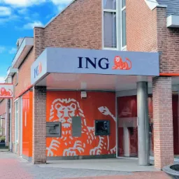 Fasada budynku banku w Toruniu z logo lwa w kolorze pomarańczowym, widoczne bankomaty i wejście.