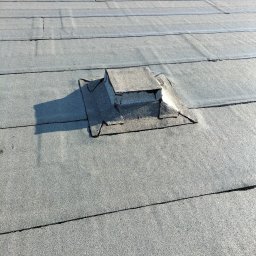 FHU LIVQUR Piotr Golus - Płaski dach pokryty papą z widocznymi łączeniami i elementami wentylacyjnymi, jeden z nich z metalowym zabezpieczeniem.