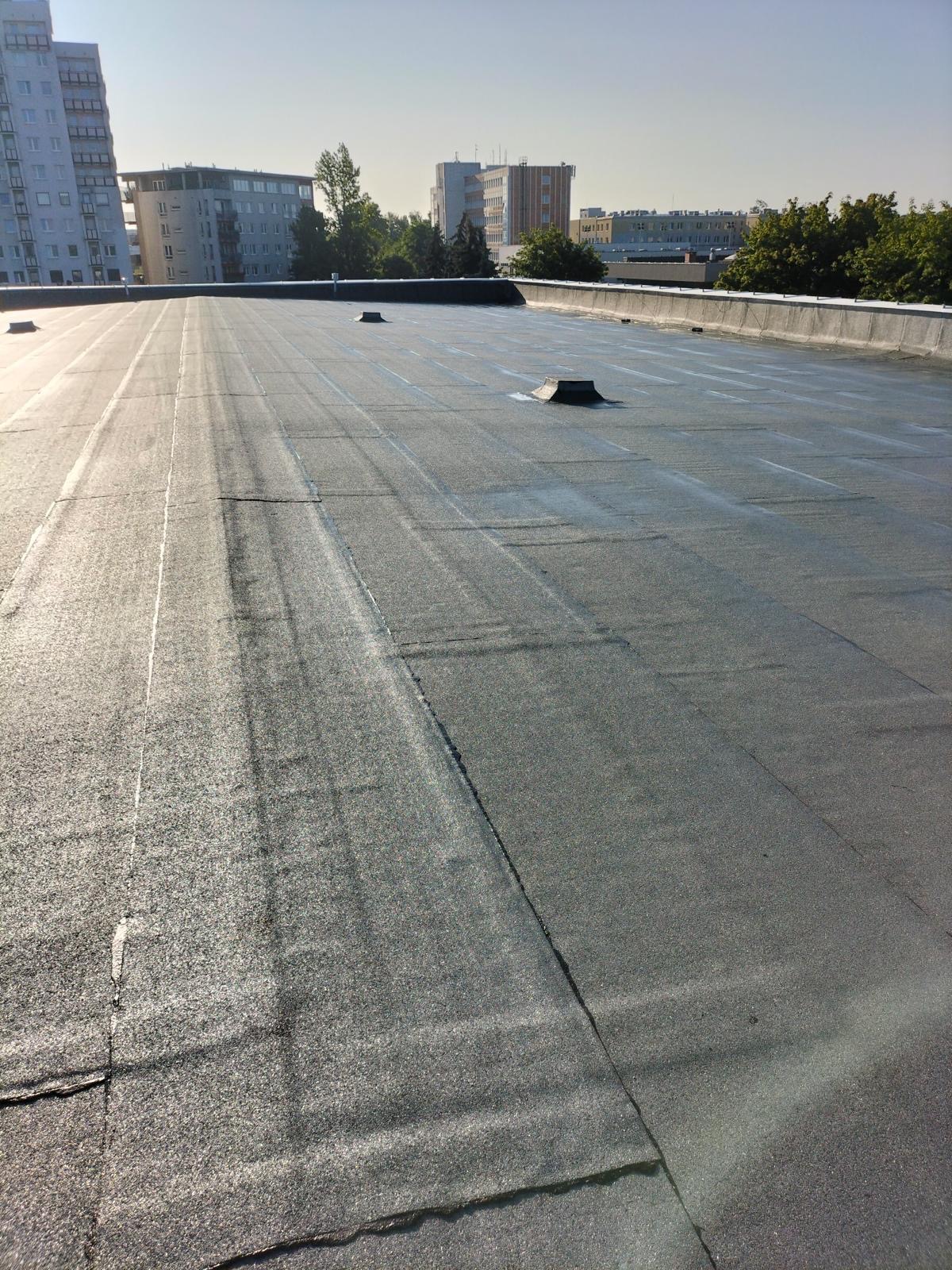 Nowe, płaskie pokrycie dachu papą termozgrzewalną w Świerczyńcu, z widocznymi kominkami wentylacyjnymi i budynkami w tle.