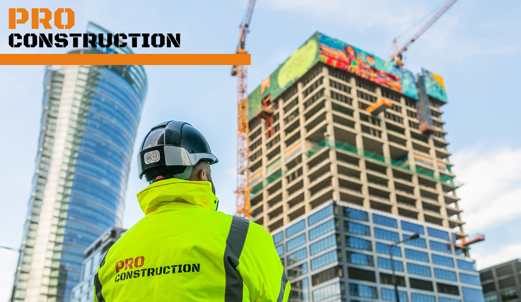 Pracownik w kasku i jaskrawej kurtce z logo firmy budowlanej na tle szkieletu budynku w budowie i nowoczesnego wieżowca.