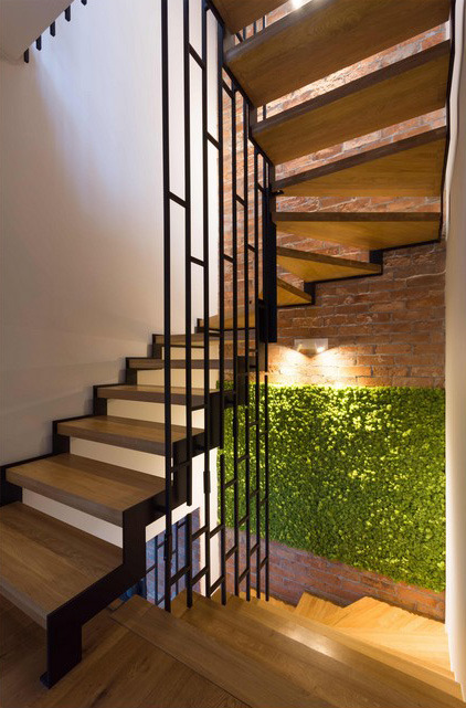 Drewniane schody z czarną metalową balustradą, ceglana ściana z panelem z mchu i oświetleniem punktowym.