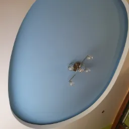 Owalny sufit podwieszany w kolorze błękitu z nowoczesnym chromowanym żyrandolem z kulistymi kloszami, otoczony białym obramowaniem, widok z dołu.