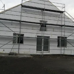 Dom w trakcie ocieplania styropianem, widoczne rusztowania i szare niebo w tle.