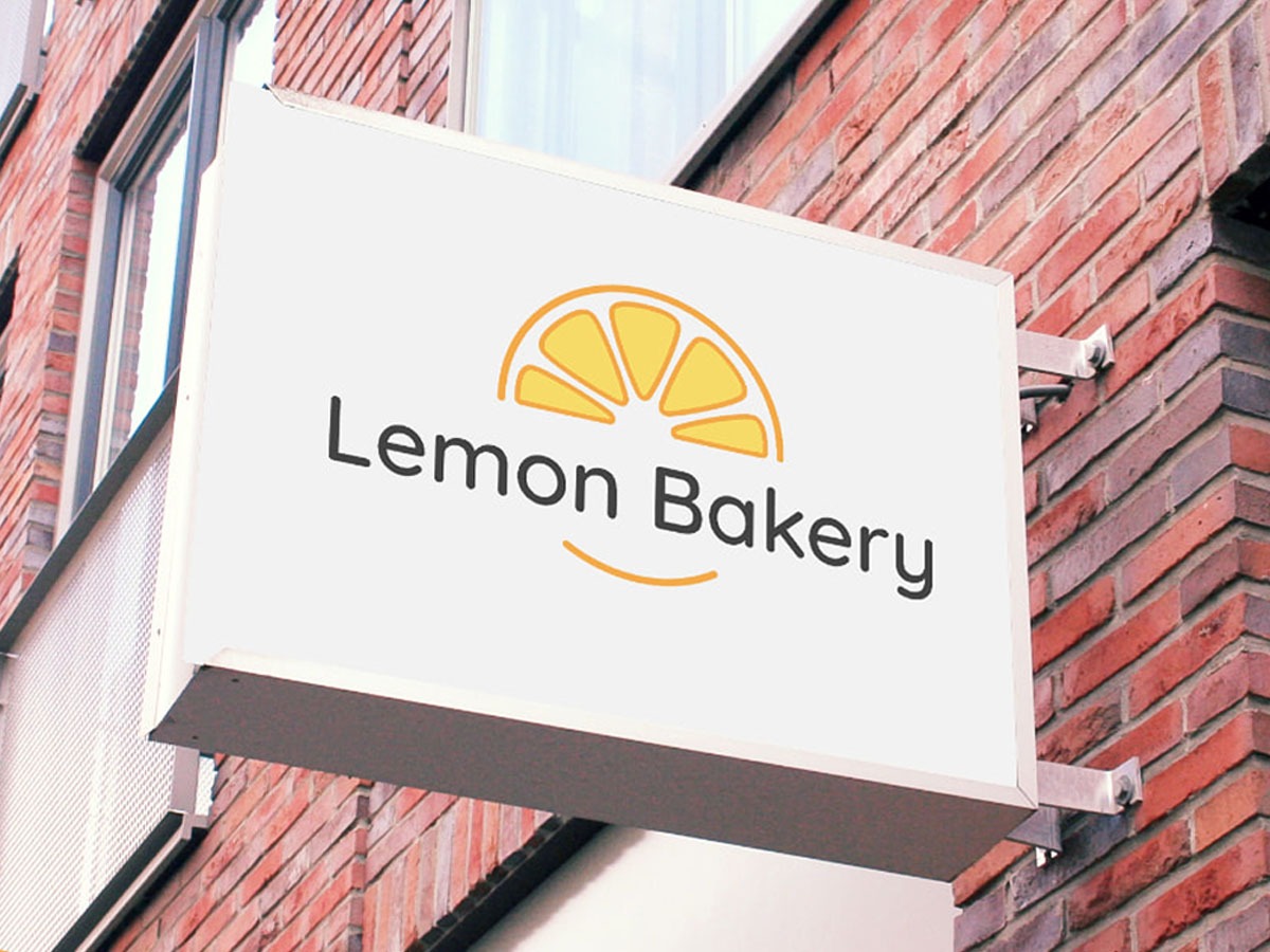 Szyld reklamowy z logo Lemon Bakery na ceglanej ścianie budynku, podświetlony od góry.