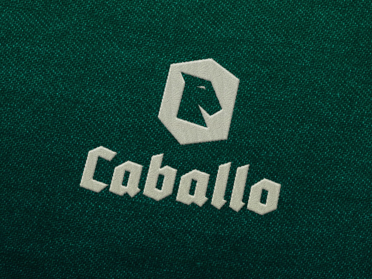 Wyhaftowane logo firmy 'Caballo' na ciemnozielonym, teksturowanym tle materiału.
