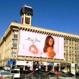 Duży baner reklamowy z wizerunkiem kobiety i perfum Miss Dior umieszczony na budynku w centrum miasta, widok z ulicy w słoneczny dzień.