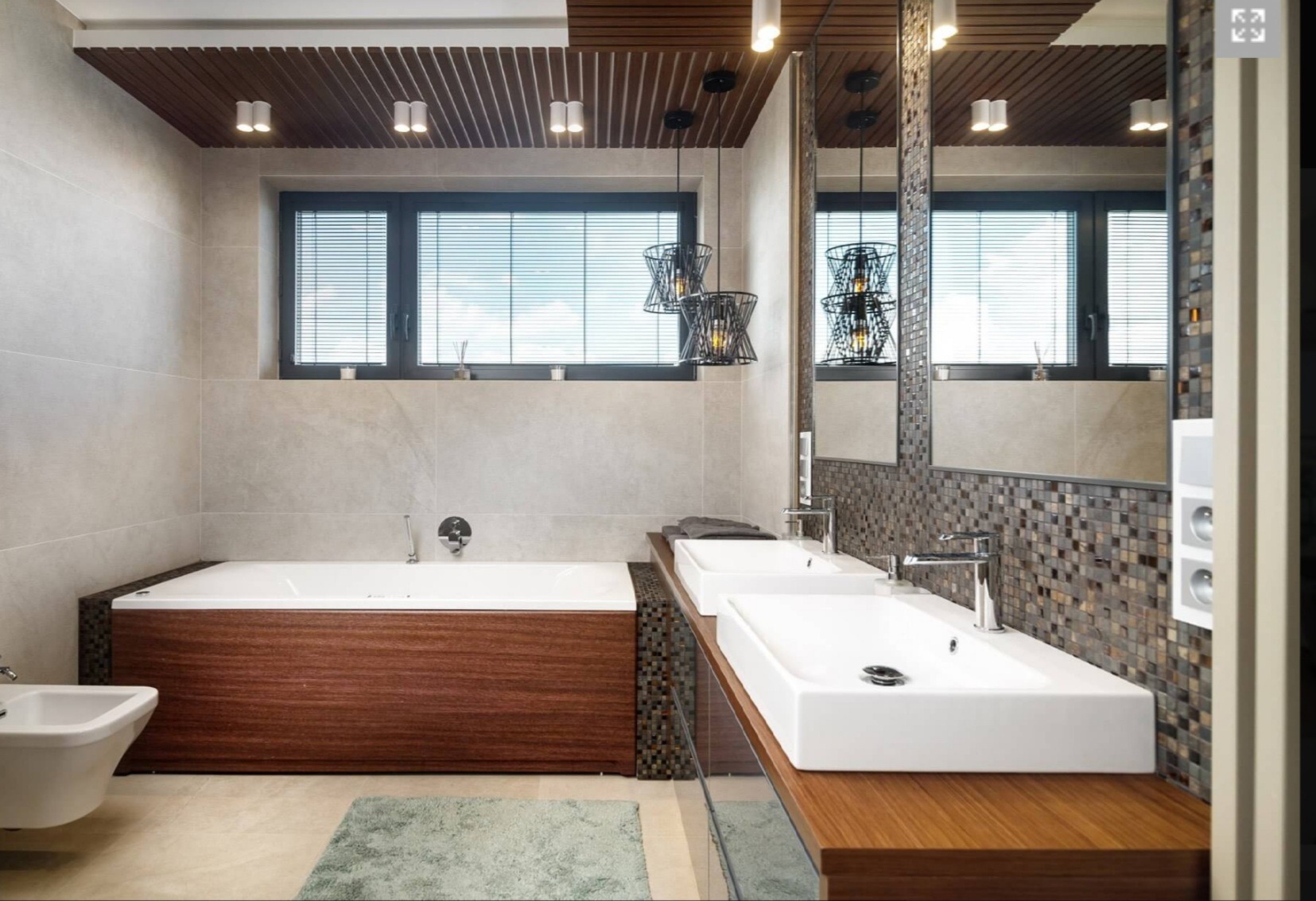 Nowoczesna łazienka z drewnianymi elementami: obudowa wanny z ciemnego drewna, blat pod umywalkami z jasnego drewna, mozaika na ścianie, wiszące lampy o geometrycznym kształcie, okno z żaluzjami.