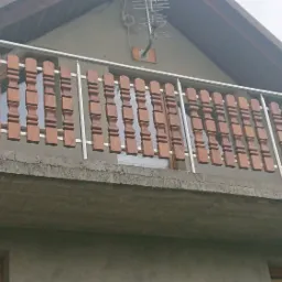 Balkon z drewnianymi, dekoracyjnymi elementami wypełniającymi przestrzeń między poziomymi, metalowymi rurami.