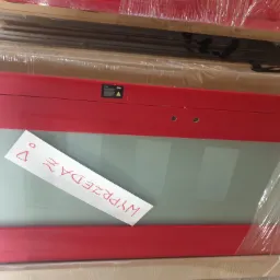 Czerwona rama z szybą, zapakowana w folię, z kartką 'WYPRZEDAŻ' napisaną odręcznie czerwoną czcionką, leżąca na palecie.