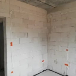 Surowy stan: Kable elektryczne prowadzone po ścianach z betonu komórkowego w nowym domu, widoczne puszki instalacyjne i peszle.