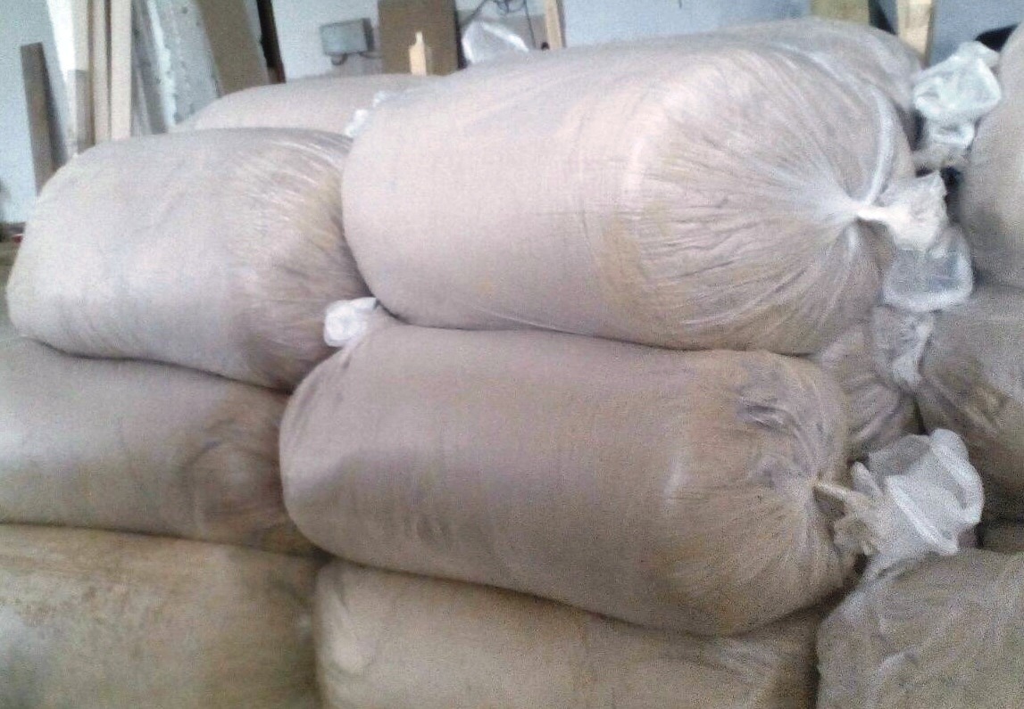 Stos worków z zawartością o jasnej barwie, prawdopodobnie przeznaczonych do transportu lub magazynowania, widoczne na tle elementów konstrukcyjnych budynku.