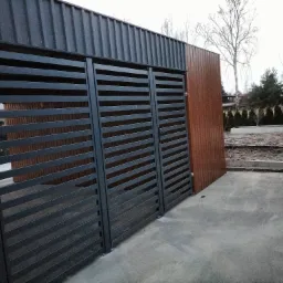 Nowoczesna, metalowa brama wjazdowa z poziomymi szczeblami, wkomponowana w ogrodzenie z paneli pionowych, widoczna z boku na betonowym podłożu.