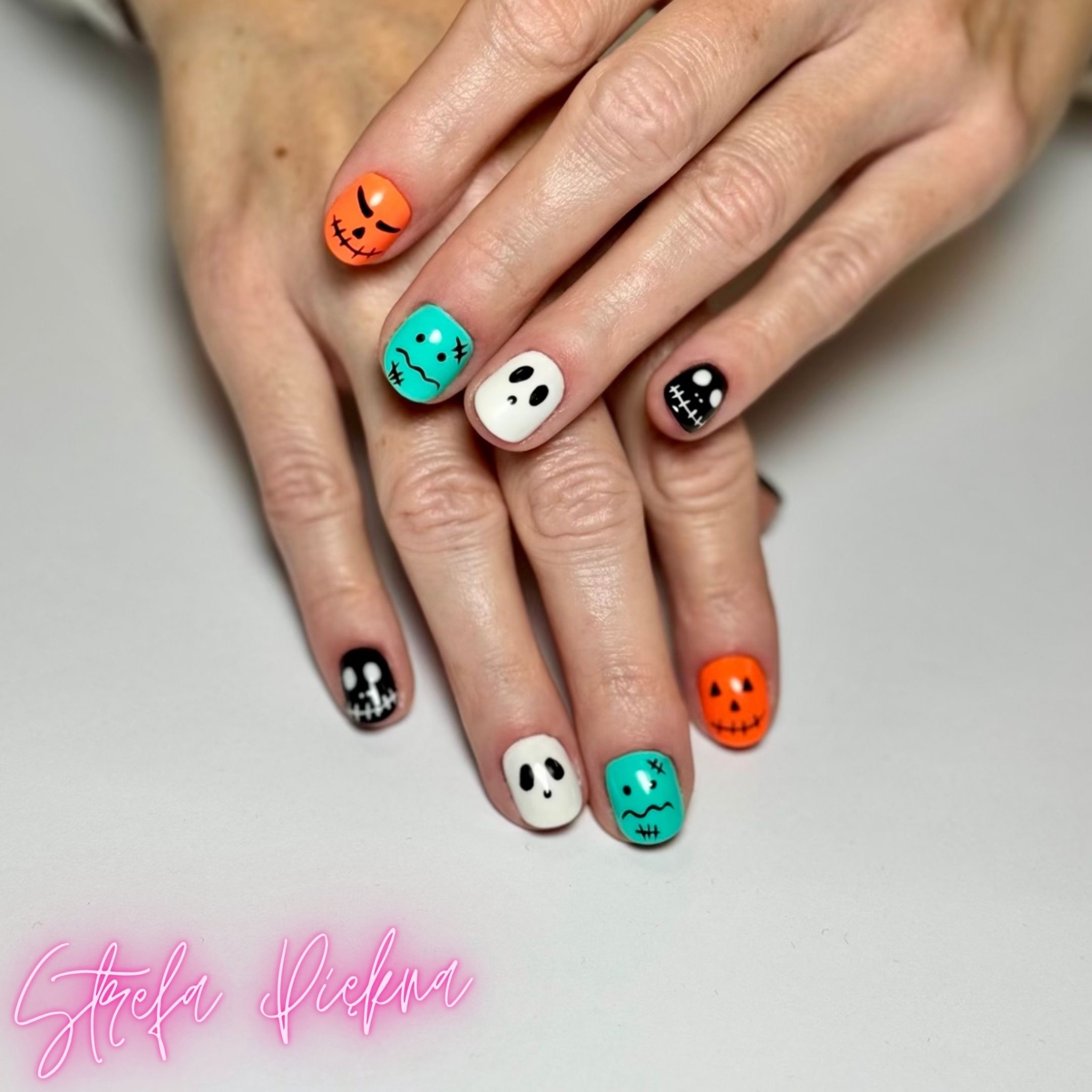 Dłonie z halloweenowym zdobieniem paznokci: dynie, duchy i potwory na krótkich, kwadratowych paznokciach na białym tle.