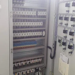 Otwarta szafa sterownicza z widocznymi licznymi przewodami, bezpiecznikami i elementami elektrycznymi, oświetlona silnym światłem z góry.