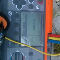 Miernik Sonel PI-520, leżący na kamiennej powierzchni z trawą, wyświetla wynik pomiaru rezystancji Re=7.88Ω, z podłączonymi przewodami w kolorach czerwonym, żółtym i niebieskim.