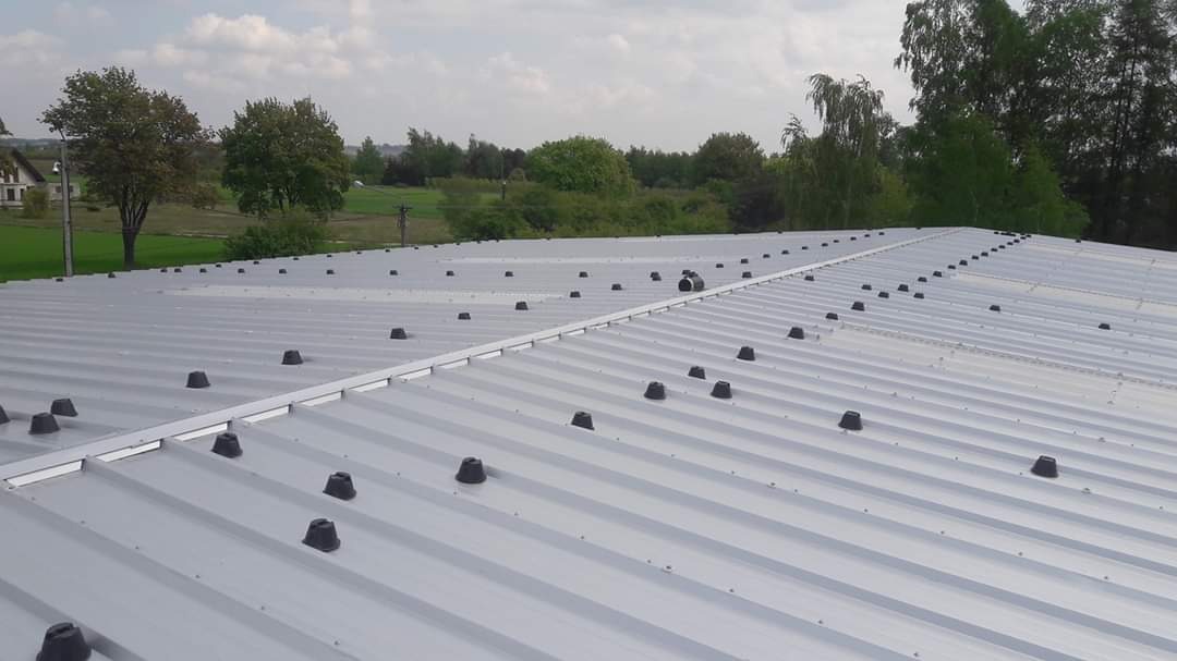 Blaszany dach z licznymi czarnymi elementami mocującymi, widok z góry na tle zieleni.