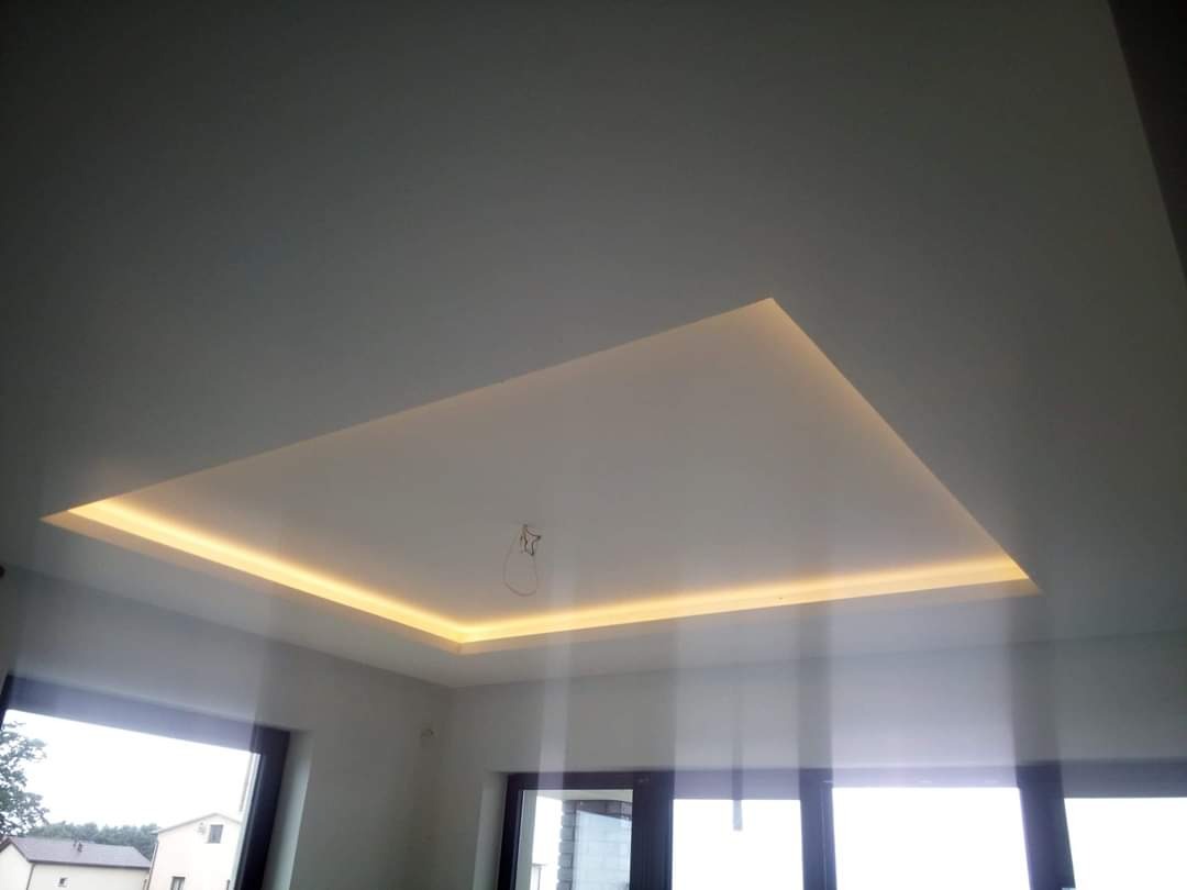 Podwieszany sufit z oświetleniem LED w kształcie prostokąta, widok z dołu na białe ściany i okna z widokiem na zewnątrz.