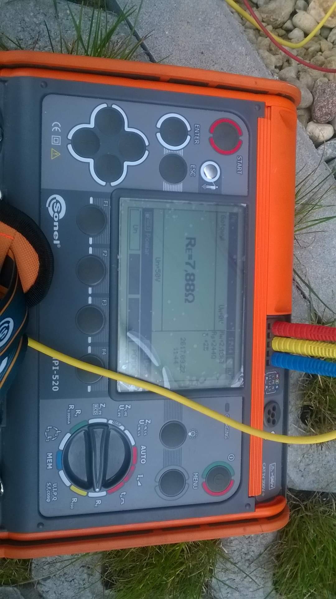 Miernik Sonel PI-520, leżący na kamiennej powierzchni z trawą, wyświetla wynik pomiaru rezystancji Re=7.88Ω, z podłączonymi przewodami w kolorach czerwonym, żółtym i niebieskim.