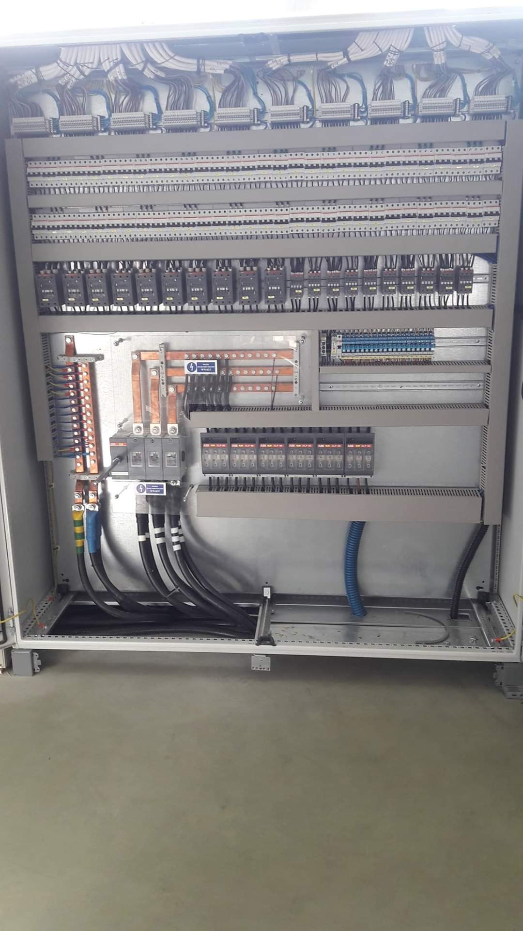 Otwarta szafa sterownicza z widocznymi licznymi przewodami, listwami zaciskowymi, bezpiecznikami i elementami łączeniowymi, uporządkowanymi wewnątrz metalowej obudowy.