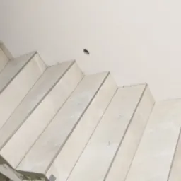 Wykończone stopnie schodów wyłożone jasnymi płytkami imitującymi marmur, widoczne ślady zaprawy i oznaczenia montażowe na ścianie.