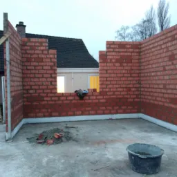 Wznoszone ściany z czerwonej cegły na fundamencie, widoczne okno w ścianie, drabina oparta o ścianę, wiadro z zaprawą na posadzce, fragment dachu domu w tle.