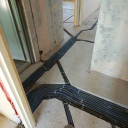 adamczak_industria - Rozprowadzenie kabli elektrycznych w peszlach, zatopionych w wylewce podłogowej podczas remontu. Widoczne korytarze i surowy stan ścian.