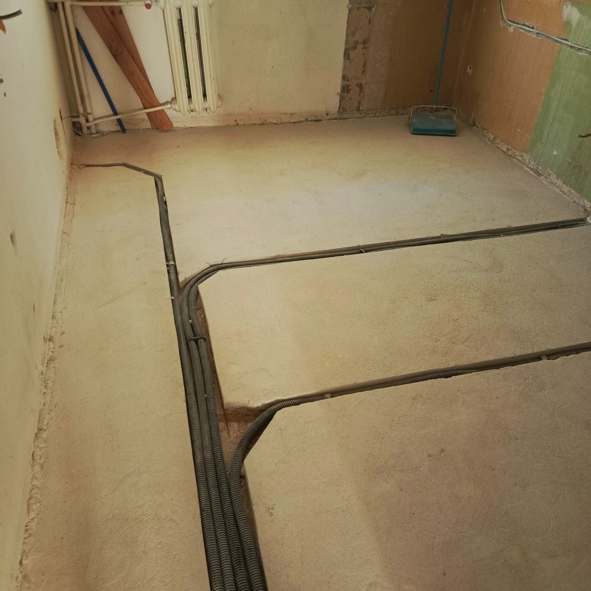 Instalacja elektryczna pod podłogą: kable w karbowanych rurach ułożone w bruzdach, przygotowane do zalania wylewką. Widok na surowy stan podłoża.
