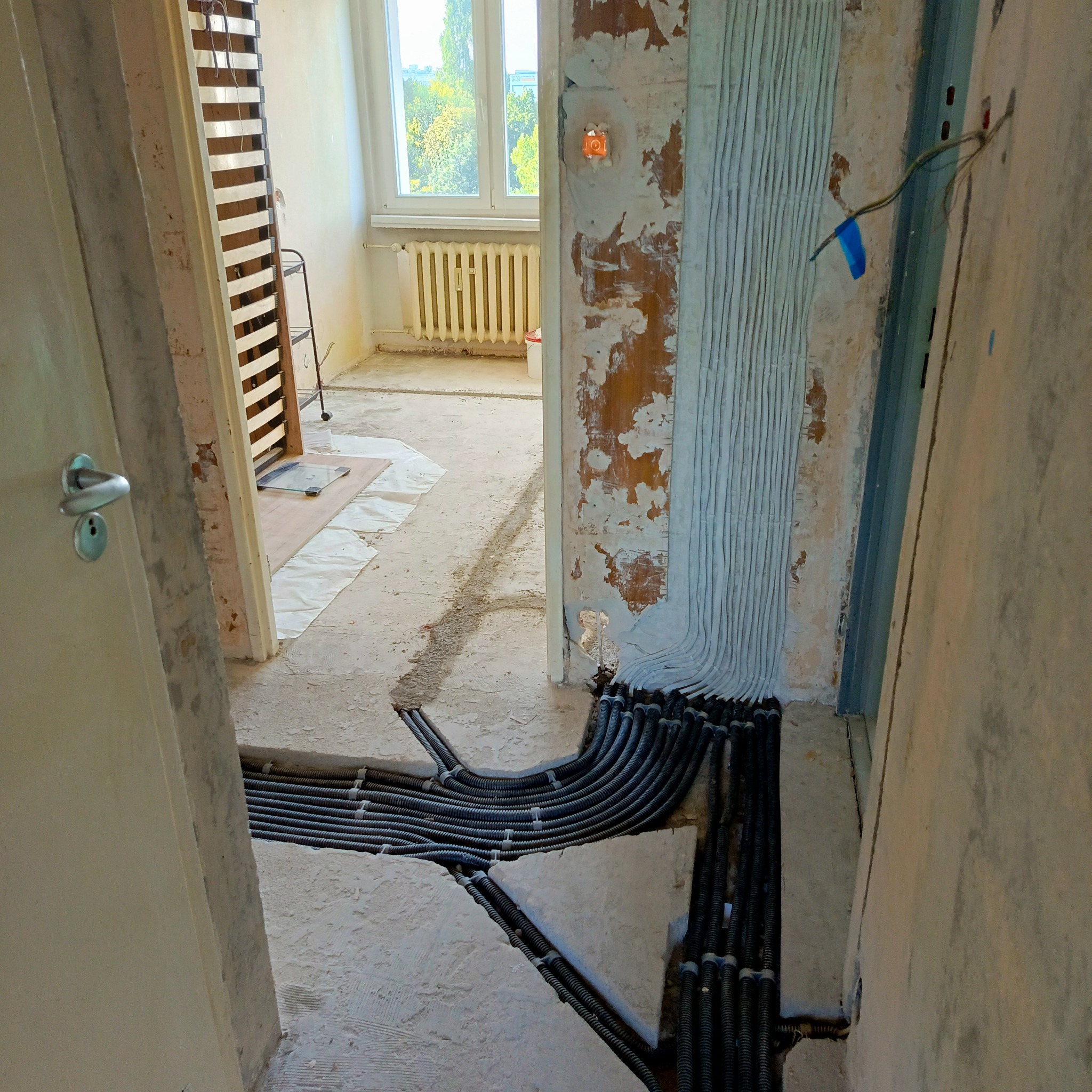 Instalacja peszli z przewodami w bruzdach ściany i podłogi w trakcie remontu. Widoczne okablowanie i przygotowane trasy podtynkowych instalacji.